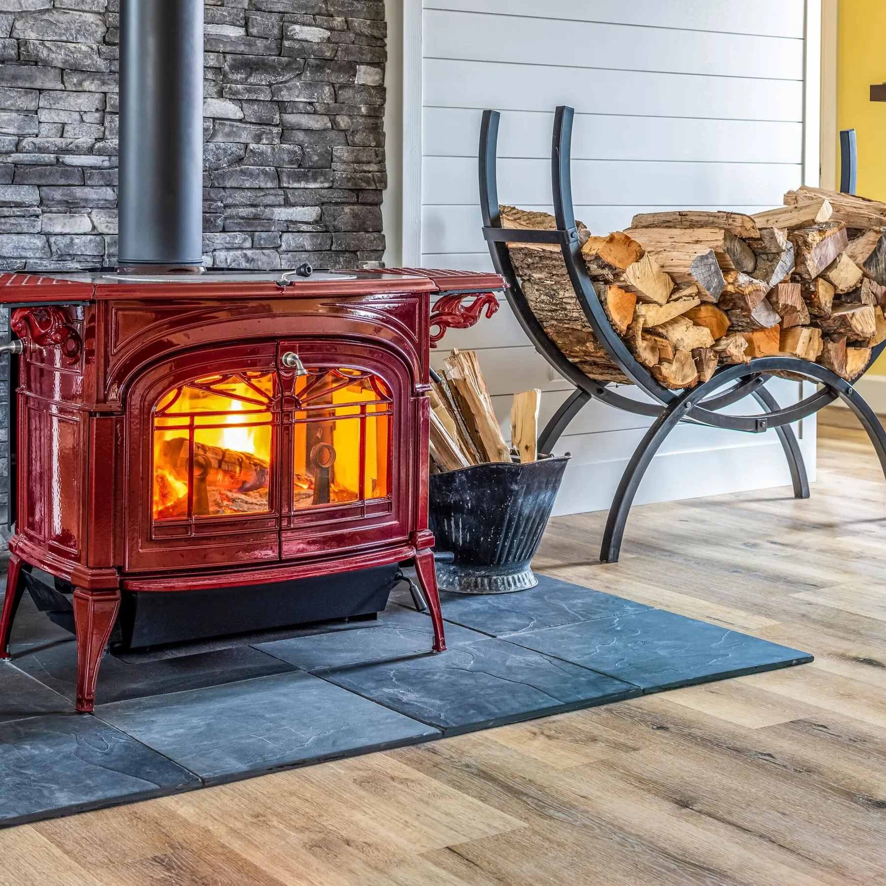 A red Vermont Castings Encore wood stove burning in a living room