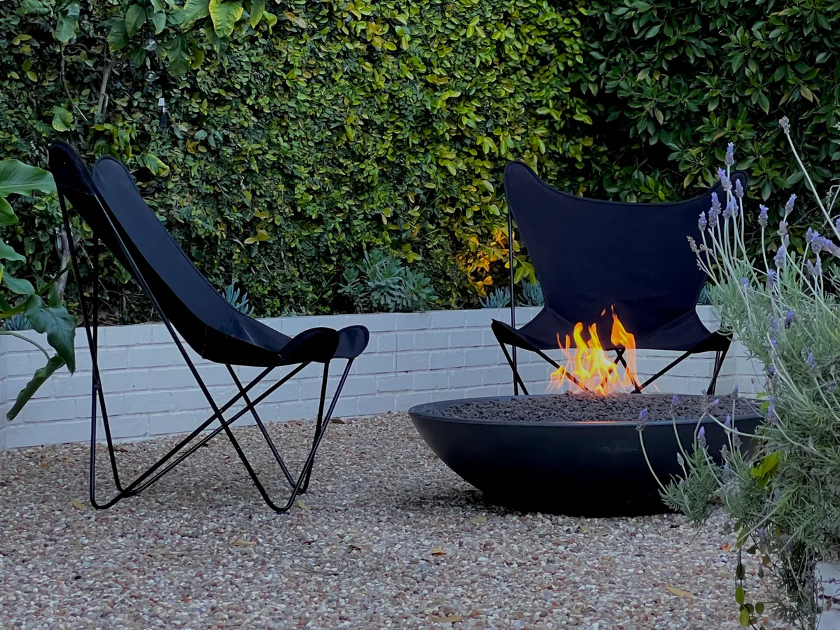 An American Fyre Designs Marseille fire bowl burning on a gravel patio