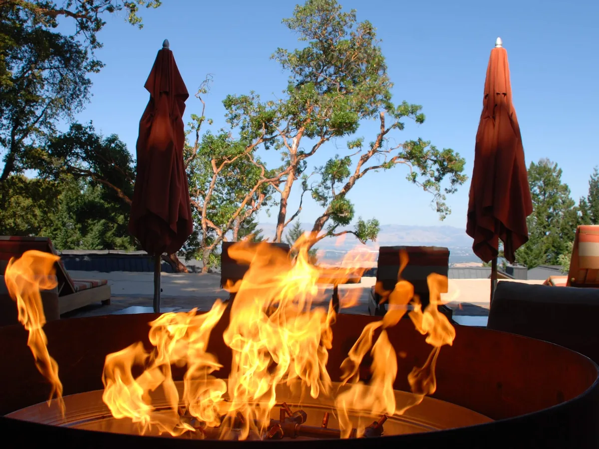 A custom gas fire pit with a Warming Trends CROSSFIRE burner burning at dusk